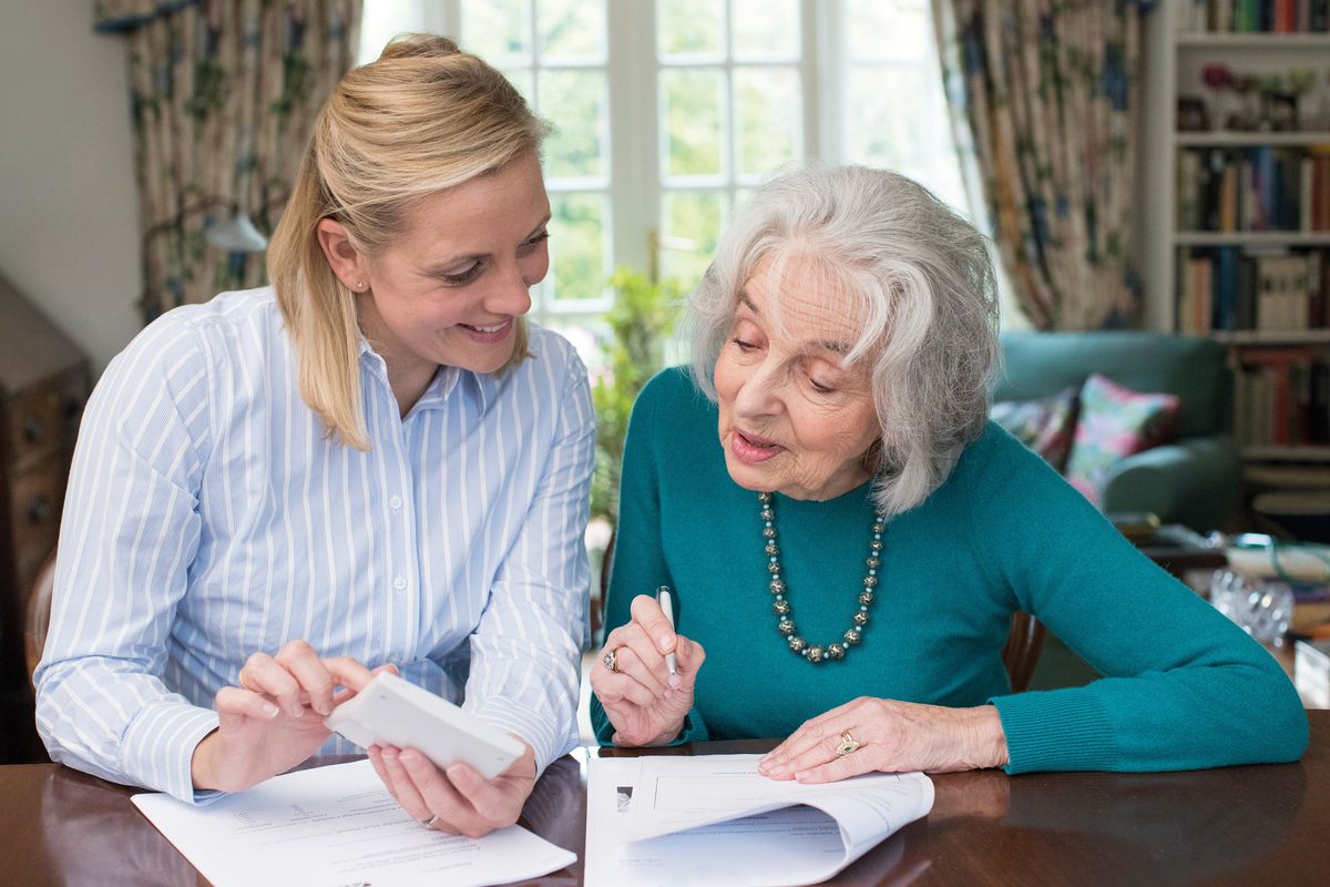 Eine junge Pflegekraft und eine ältere Frau schauen sich Vertragsunterlagen an.