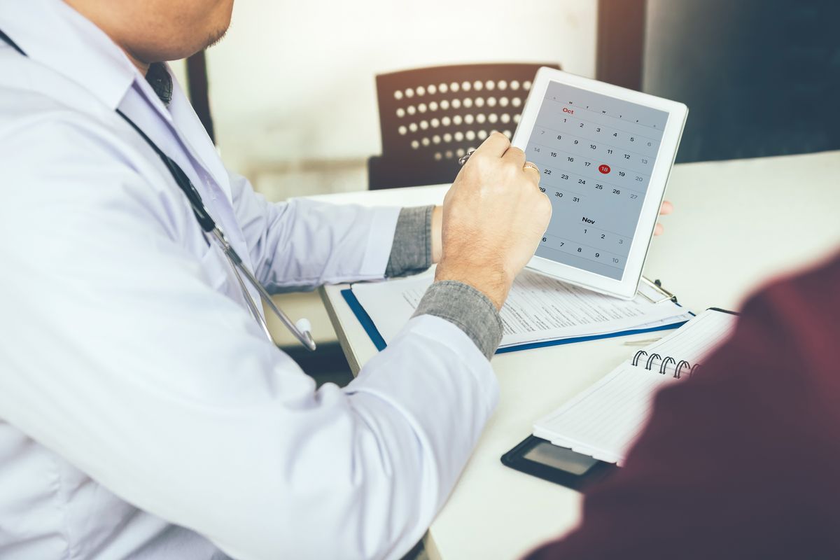Eine Person aus dem Gesundheitswesen plant auf einem Tablet-PC etwas in einem Kalender.
