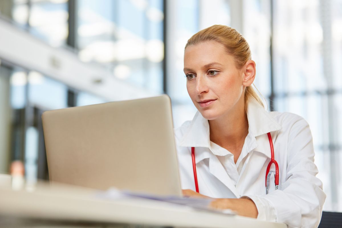 Eine Frau aus dem Gesundheitsbereich sitzt an ihrem Arbeitsplatz vor einem Notebook