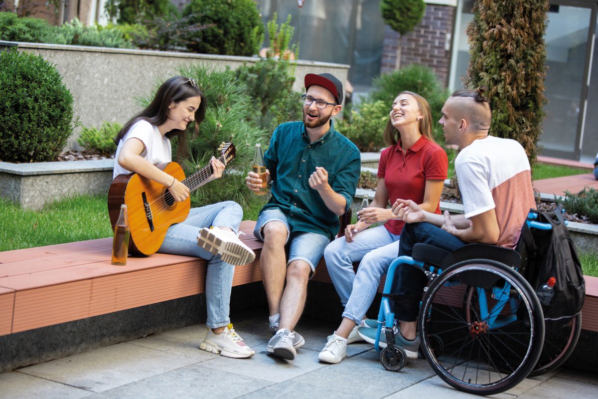 Mehrere junge Menschen von denen einer im Rollstuhl sitzt sitzen zusammen. Eine Person spielt Gitarre.