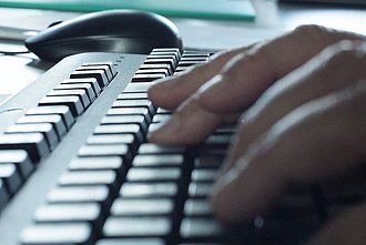 Tippende Finger auf einer Tastatur mit Computermaus im Hintergrund